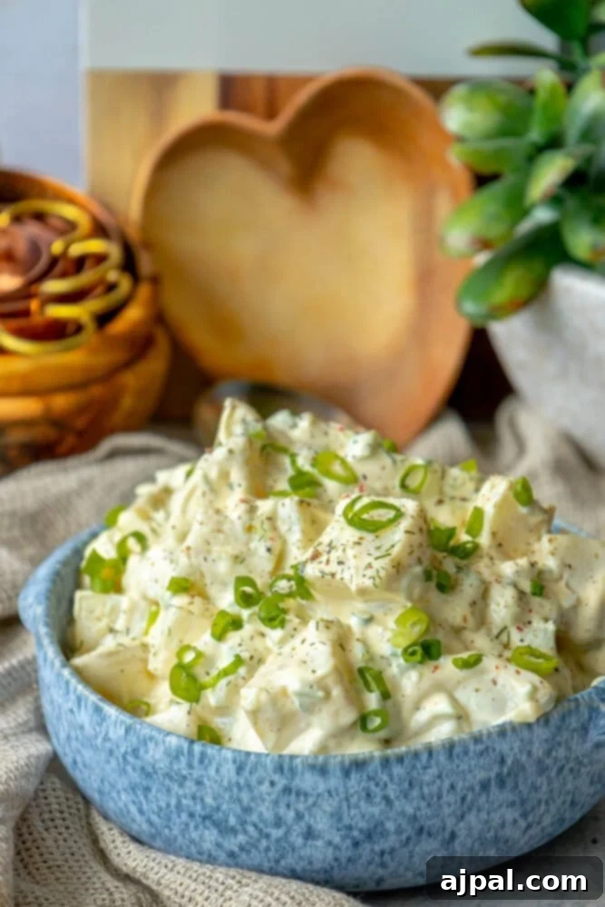 Simple & Scrumptious Potato Salad 9 Picture of creamy potato salad with green onions and cracked pepper in a blue bowl, garnished beautifully.