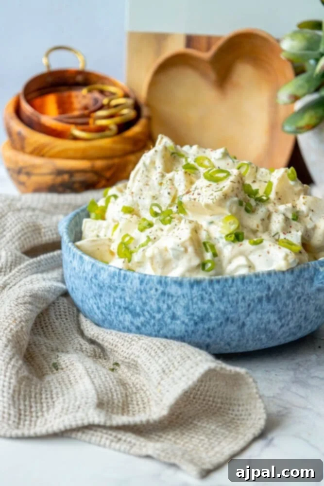 Simple & Scrumptious Potato Salad 10 Picture of creamy potato salad with green onions and cracked pepper in a blue bowl, ready for serving.