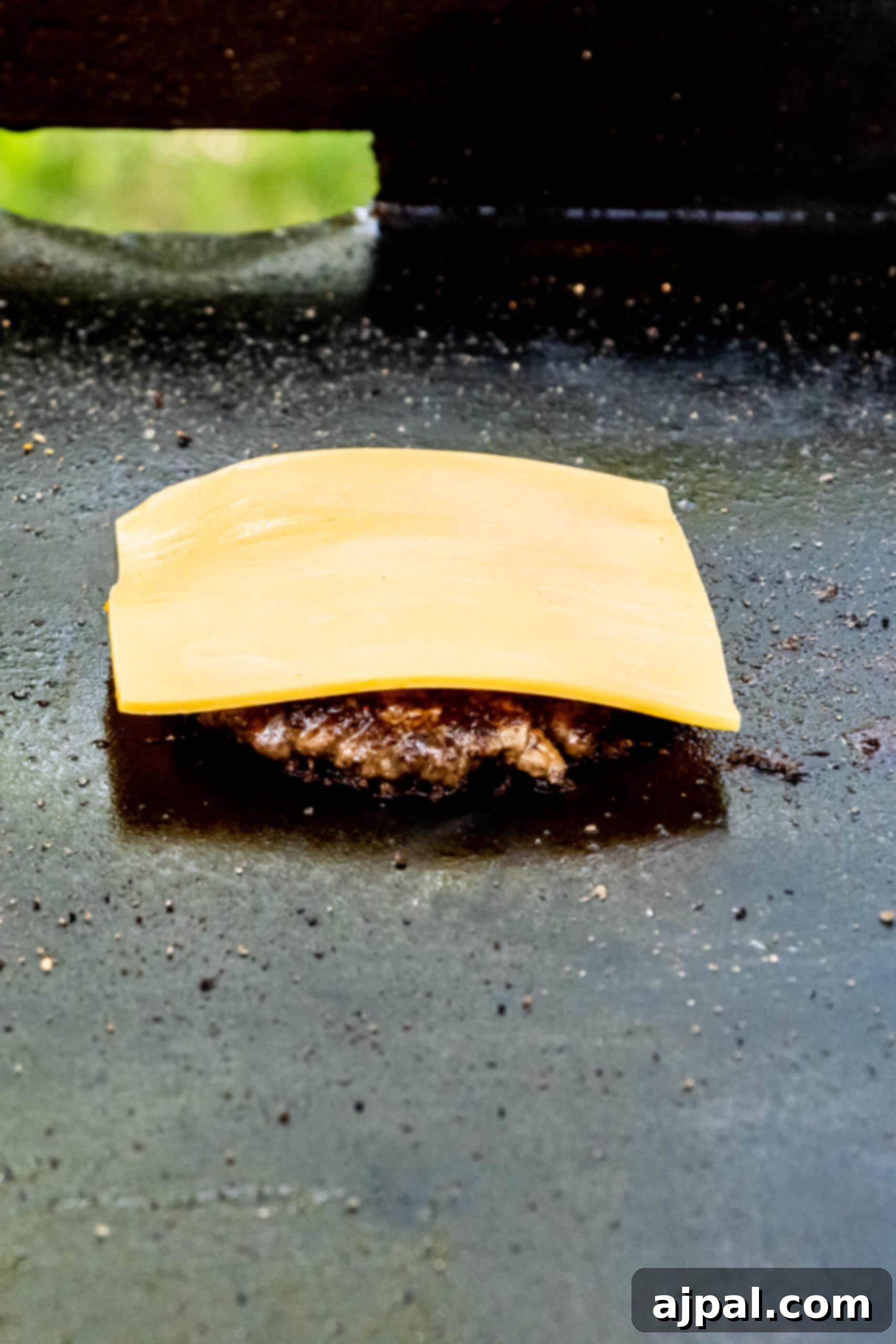 picture of slice of american cheese on a ground beef patty on a griddle