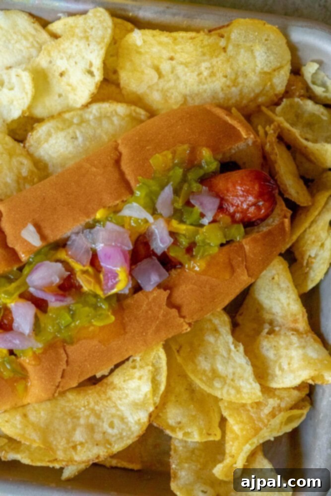 picture of bacon-wrapped hot dog in a bun topped with mustard, relish, and onions