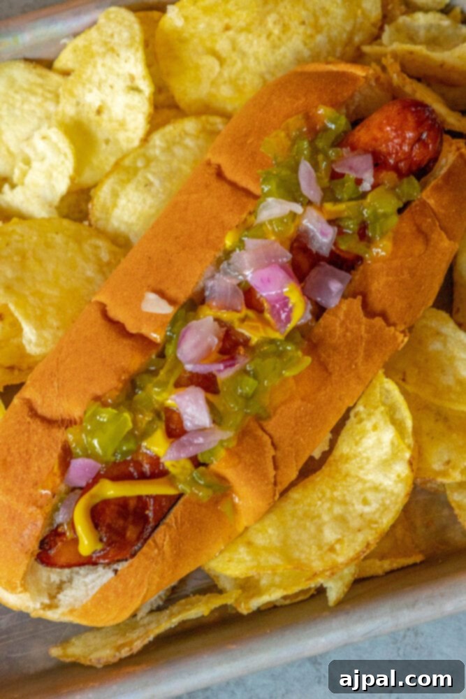 picture of bacon-wrapped hot dog in a bun topped with mustard, relish, and onions