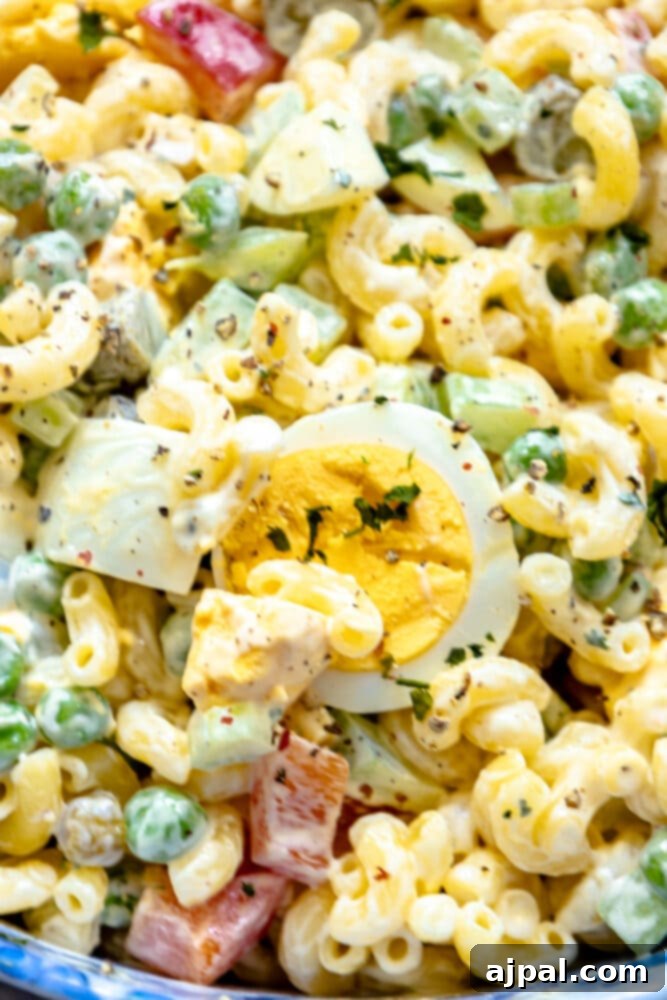 Creamy macaroni salad with visible peppers, peas, and boiled eggs in a blue serving bowl, ready for a potluck