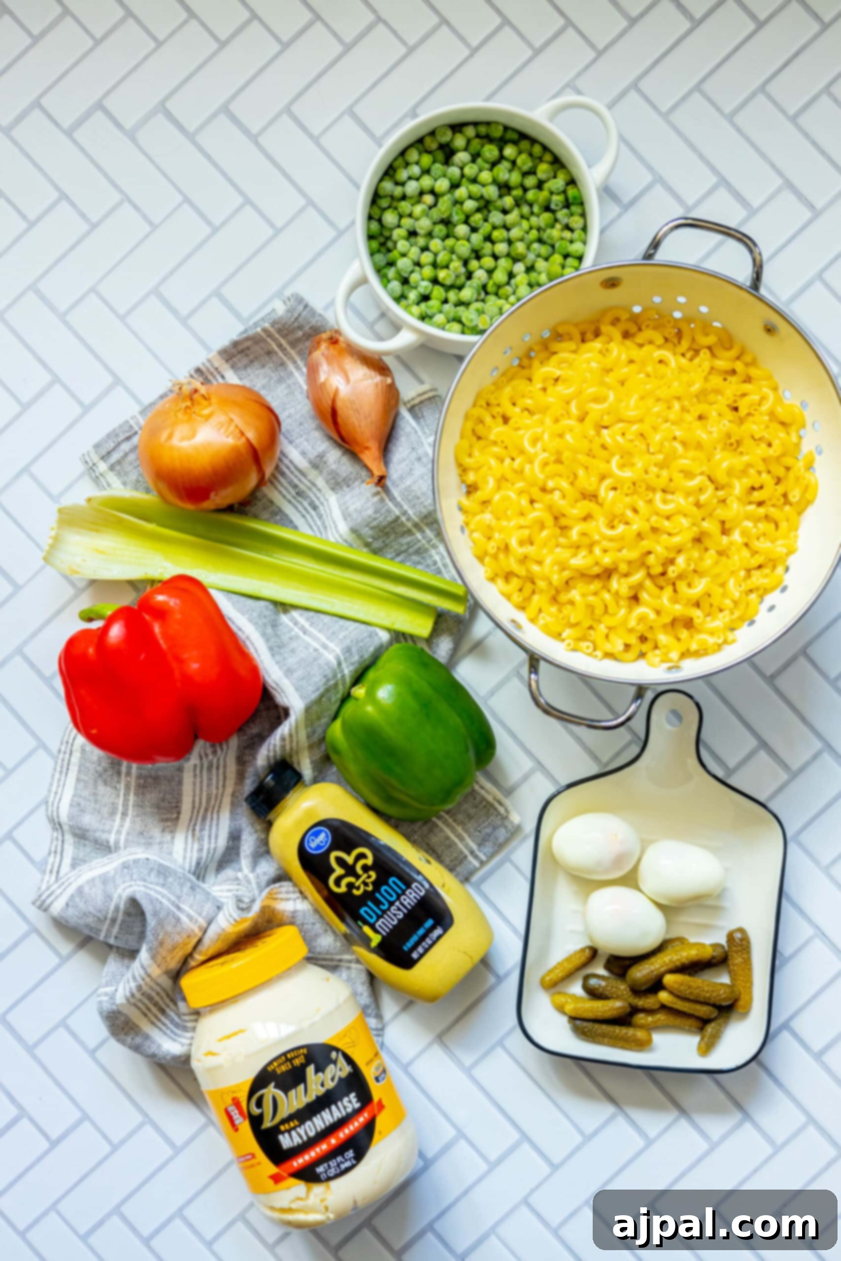 Assortment of macaroni, chopped vegetables like shallots, celery, peppers, peas, and hard-boiled eggs, alongside a bowl of dressing ingredients on a rustic table