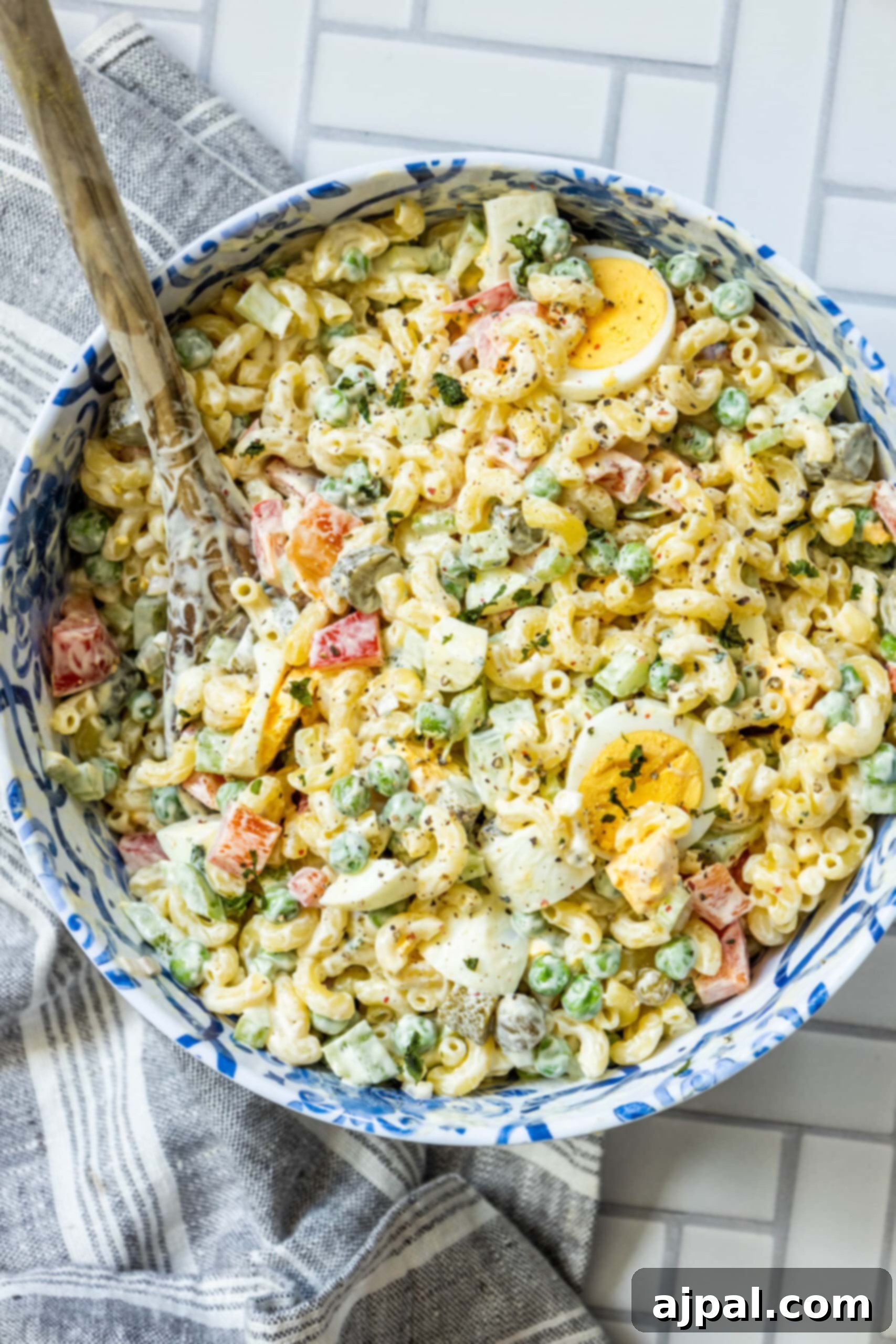 A separate bowl of creamy macaroni salad dressing, featuring mayonnaise, mustard, and spices, next to a bowl of pasta and vegetables