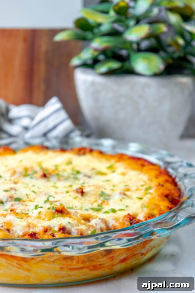 Delicious baked spaghetti pie in a glass dish, beautifully topped with golden-brown melted cheese, ready to be served on a rustic wooden table.