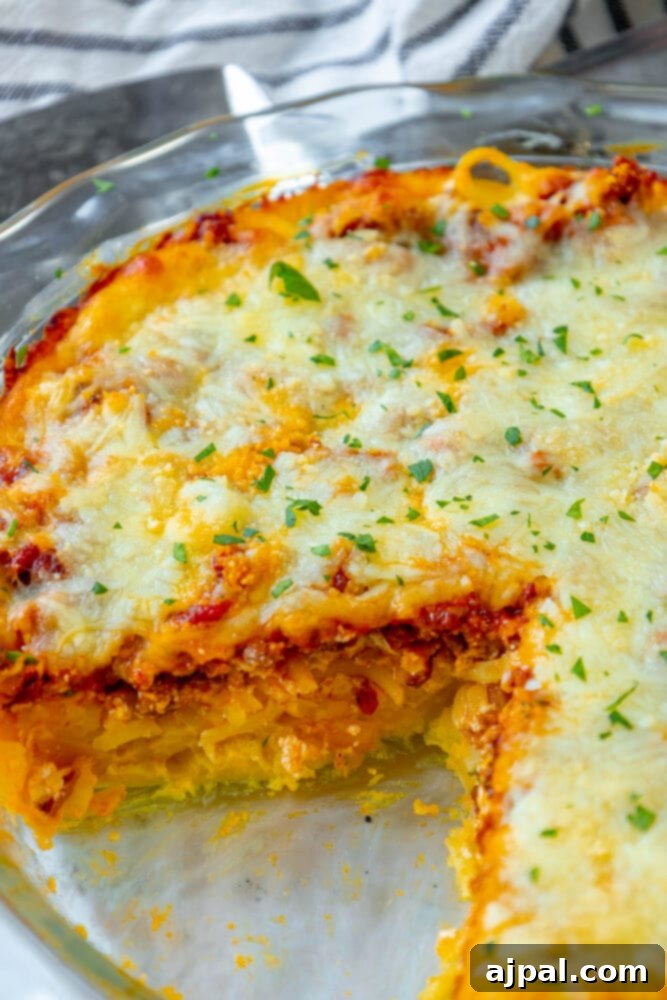 A perfectly baked slice of spaghetti pie, displaying its creamy, cheesy layers and savory meat sauce, served on a white plate with a fork.