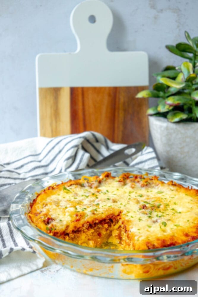 A large slice of baked spaghetti pie casserole missing from a glass dish, highlighting the inviting layers of pasta, sauce, and cheese.