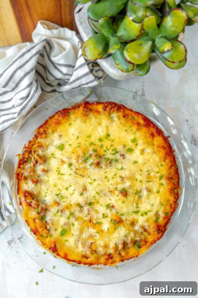A slice of baked spaghetti pie, rich with cheese and meat, served on a white plate with a side of fresh greens.