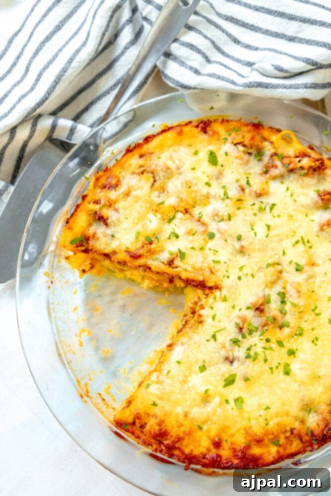A delectable cheesy spaghetti pie, freshly baked in a clear glass dish, with one slice already removed, revealing its mouth-watering layers.