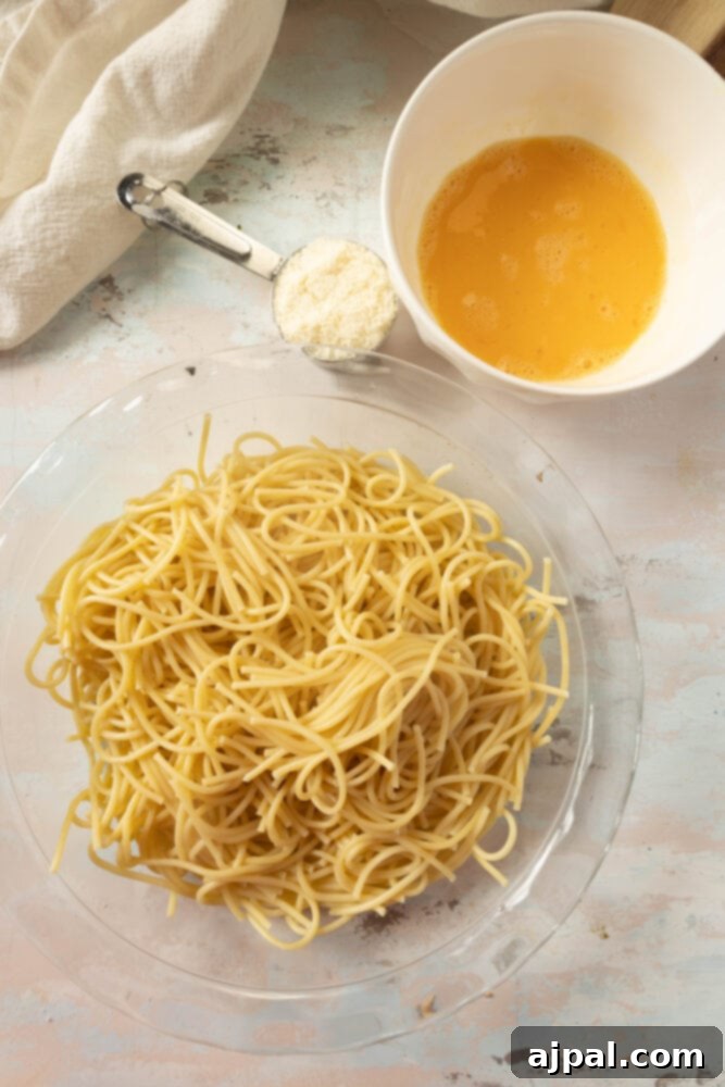 Boiled spaghetti noodles being prepared in a pie plate, with parmesan cheese and eggs ready to be mixed in for the crust.