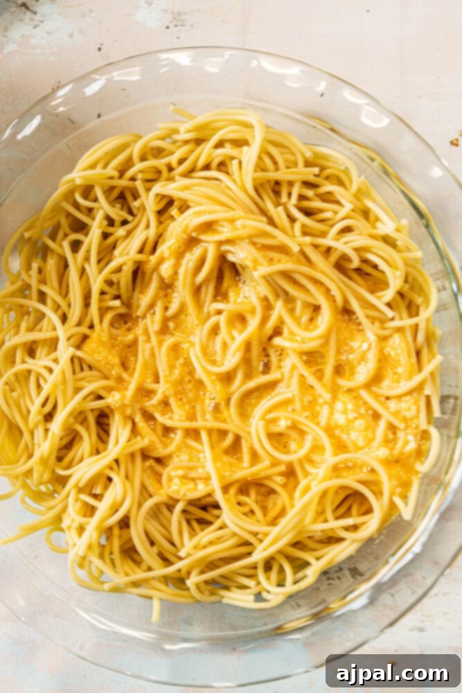 Spaghetti, eggs, and parmesan cheese already mixed together in a pie plate, forming the base of the spaghetti pie.