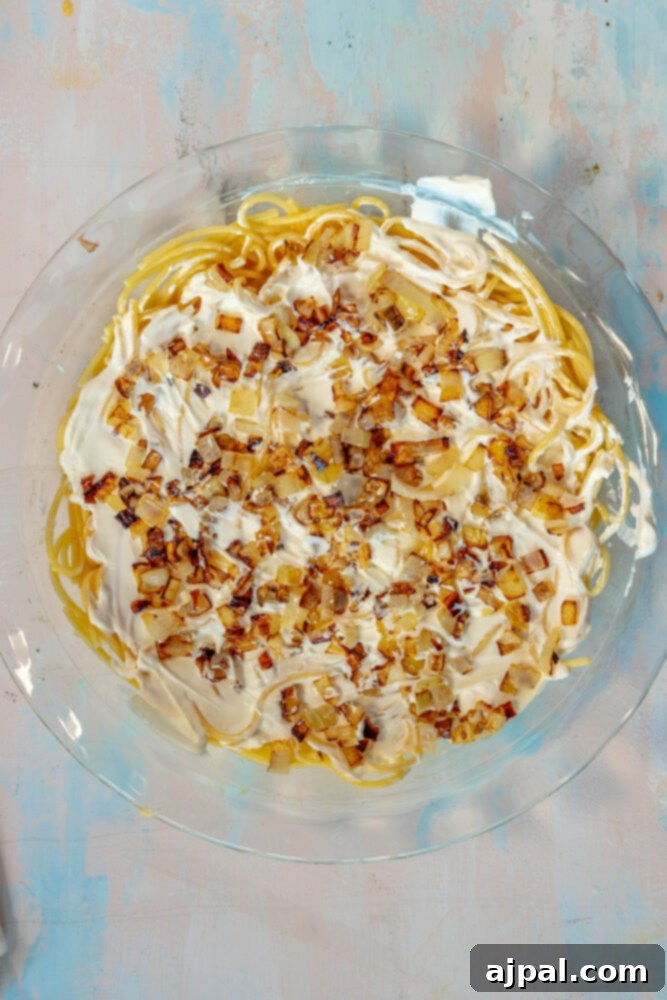 The spaghetti and egg mixture topped with a creamy layer of sour cream and sautéed onions, ready for the next layer of the pie.
