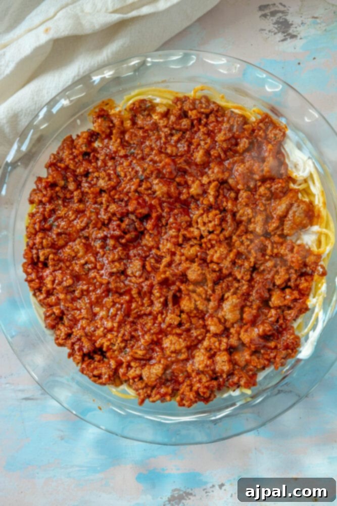 Spaghetti pie base now topped with a rich layer of cooked, crumbled meat in a savory tomato sauce, creating a delightful filling.