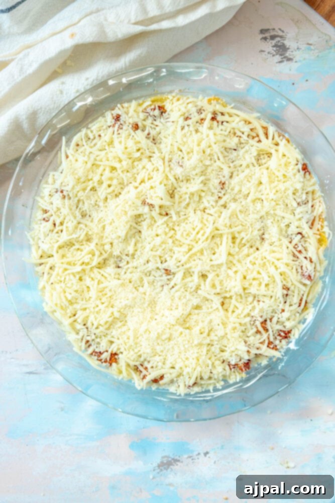 The final layer of shredded mozzarella cheese generously sprinkled over the spaghetti pie, awaiting its turn in the oven for a golden, bubbly finish.