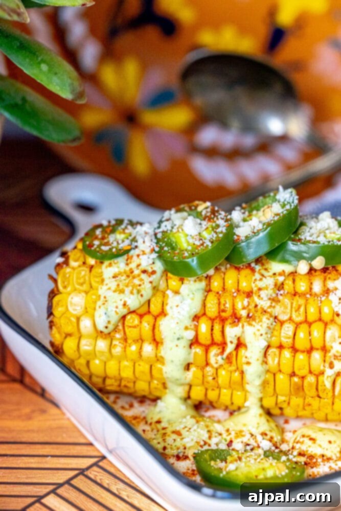 Avocado Jalapeno Elotes - a close-up of grilled corn on the cob with creamy green sauce and spicy toppings