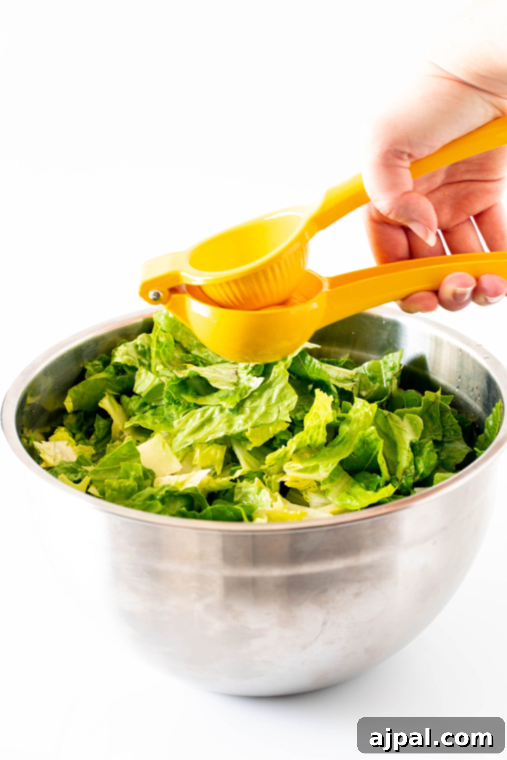Fresh lemon juice being strained over a bowl of prepped lettuce, ensuring a smooth and seed-free dressing for the salad.