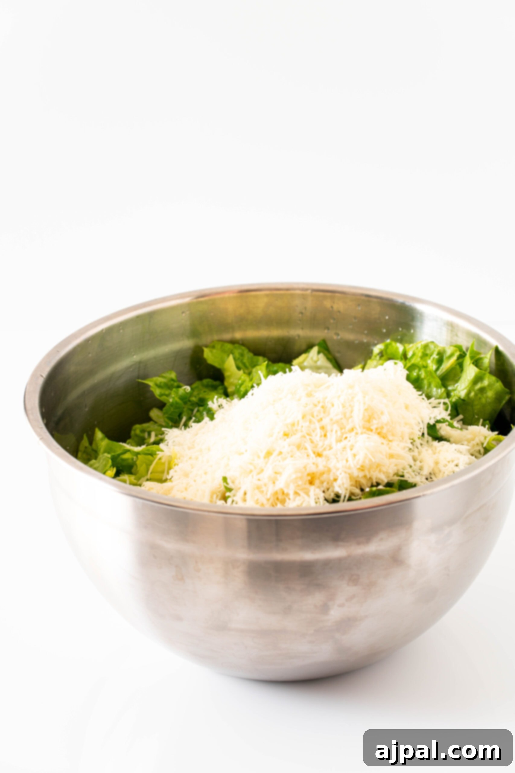 Finely grated Parmesan cheese being sprinkled generously over a bed of fresh romaine lettuce, ready to be tossed with the zesty lemon dressing.