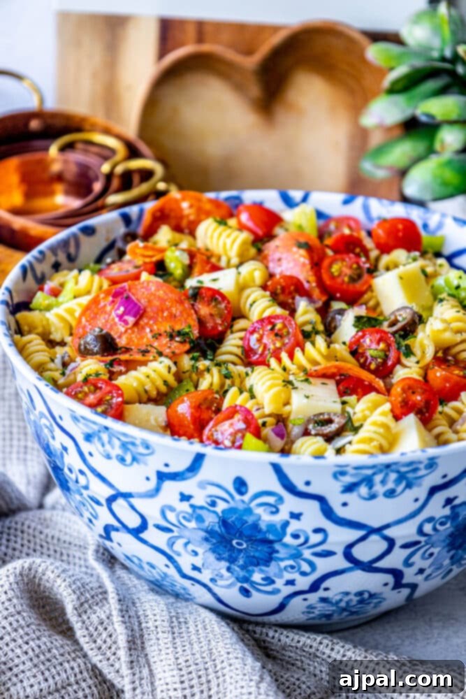 picture of pasta salad with pepperoni, olive, tomatoes, onions, cubes of mozzarella cheese, and bell peppers in a blue bowl 