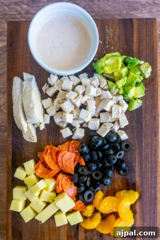 picture of cooked chicken breast, avocado, pepperoni, cheese, olives, and mandarin oranges on a cutting board