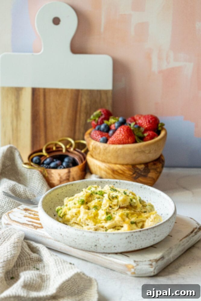 No-Fuss Chicken Tetrazzini 11 A bowl of creamy chicken tetrazzini with peas and a side of fresh berries on a wooden cutting board.