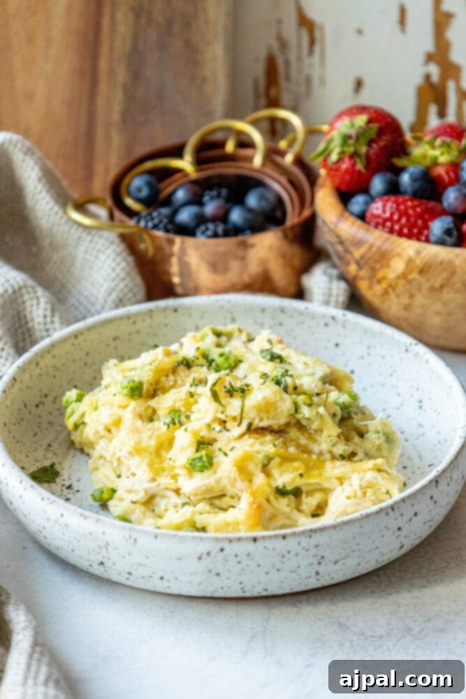 A plate of golden-baked chicken tetrazzini with peas, next to a small bowl of mashed potatoes and fresh berries on a rustic wooden cutting board.