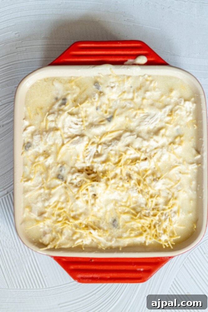 A baking dish containing a mix of egg noodles, shredded chicken, and green peas, ready for the creamy sauce to be added.