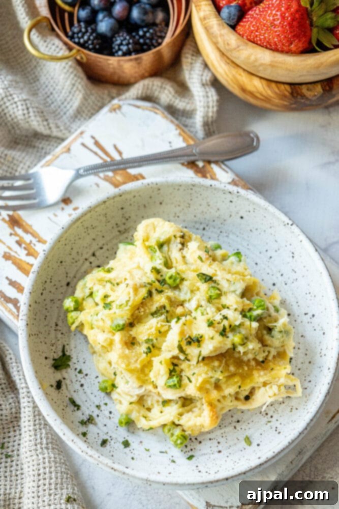 A serving of baked chicken tetrazzini noodle casserole with peas on a white plate, positioned next to a bowl of fresh berries, creating a balanced and inviting meal.