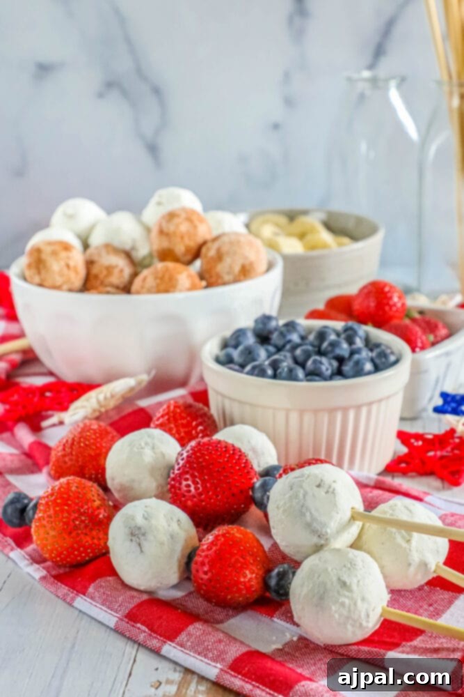 Red, White, and Blue Dessert Skewers 2 A hand holding a vibrant red, white, and blue dessert kabob with a donut hole, fresh blueberries, and sliced strawberries.