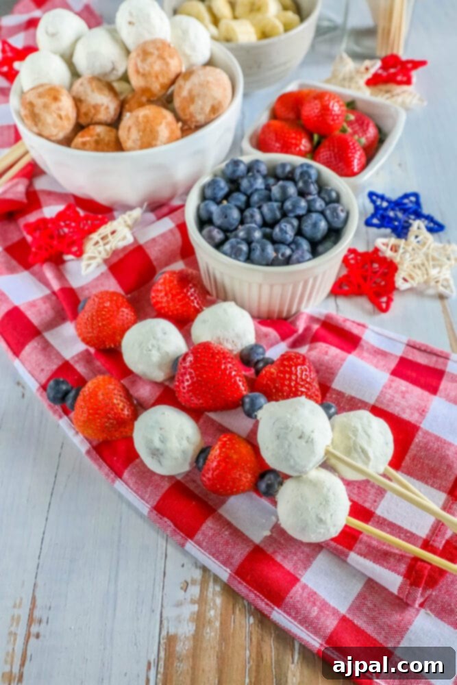Red, White, and Blue Dessert Skewers 7 A close-up of a hand holding a perfectly arranged red, white, and blue dessert kabob with a donut hole, blueberries, and strawberries, ideal for a 4th of July celebration.