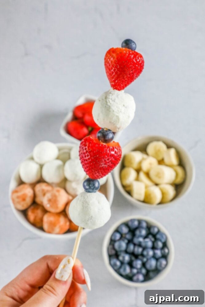 Red, White, and Blue Dessert Skewers 3 A person holding a red, white, and blue dessert kabob with strawberries, blueberries, and a donut hole, ready to be enjoyed.