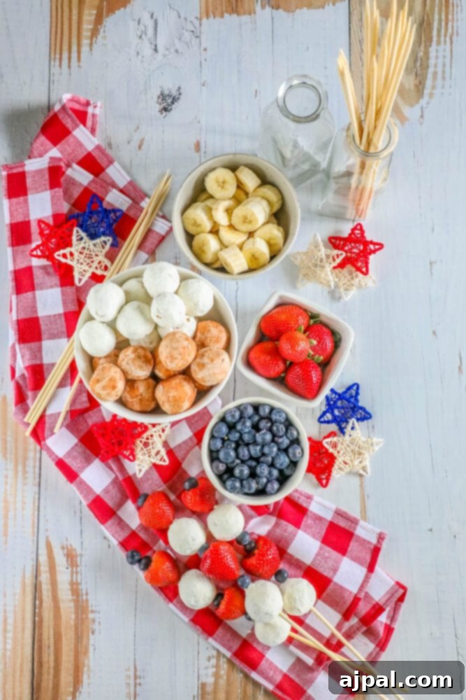 Red, White, and Blue Dessert Skewers 4 A hand holding a festive red, white, and blue dessert kabob with a donut hole, blueberries, and strawberries on a wooden table.