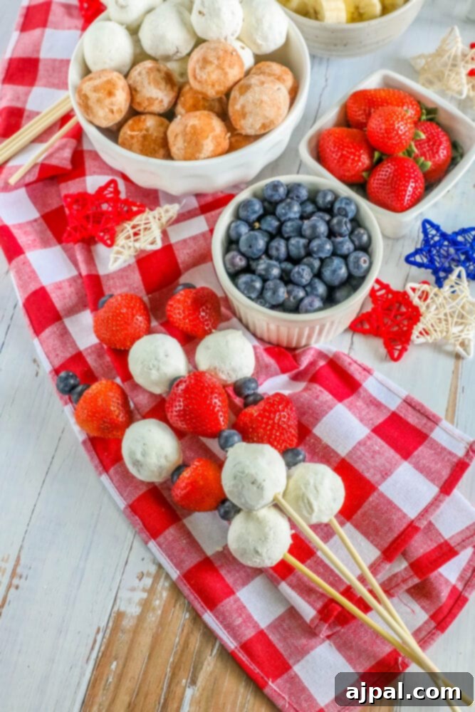 Red, White, and Blue Dessert Skewers 6 A hand holding a perfectly assembled 4th of July dessert kabob, featuring a donut hole, fresh blueberries, and vibrant strawberries, a delightful summer treat.