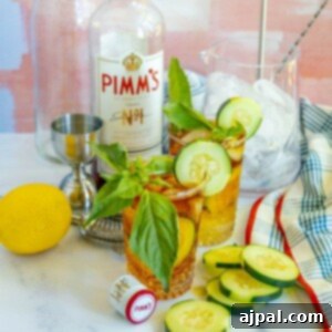 Two Pimm's Cup cocktails in front of a bottle of Pimm's, with sliced cucumbers on the table, showcasing a delightful summer drink.