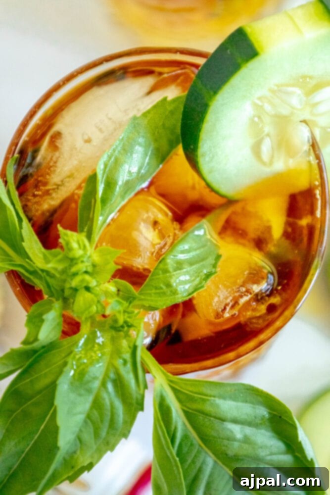 A chilled Pimm's Cup cocktail in a glass, beautifully garnished with fresh cucumber slices and basil leaves, ready to be enjoyed.