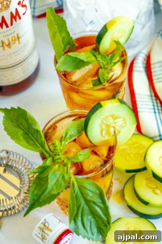 A close-up of a Pimm's Cup cocktail, showcasing the vibrant colors of cucumber and basil garnishes against the dark reddish liqueur, evoking a refreshing and elegant summer drink.