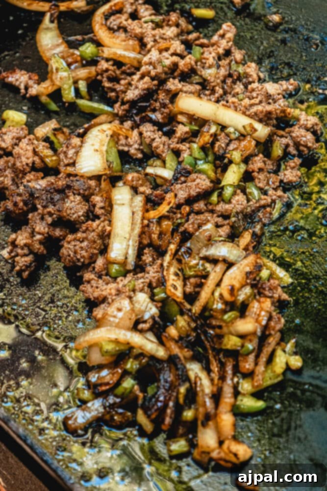 Chopped ground beef, peppers, and onions cooking on a blackstone griddle.