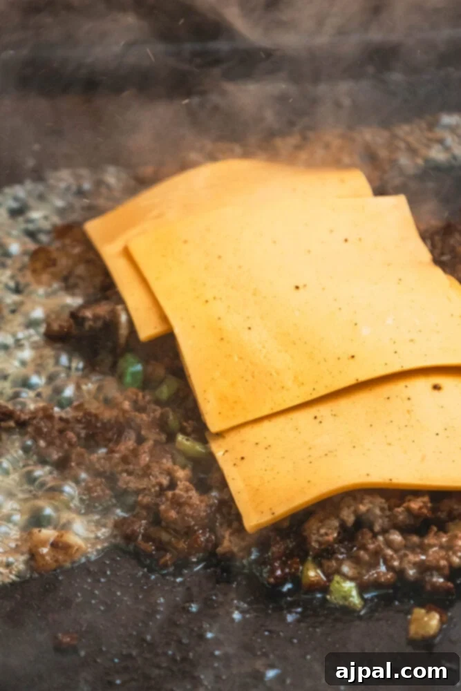 Chopped ground beef, peppers, and onions covered with slices of American cheese melting on the griddle.