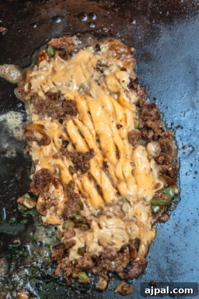 Melted American cheese bubbling over the chopped beef and vegetable mixture on the griddle.
