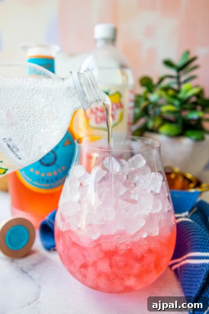 Sunset Sip Blood Orange Gin Tonic 7 Pink gin with simple syrup in a glass with ice, and tonic being poured.