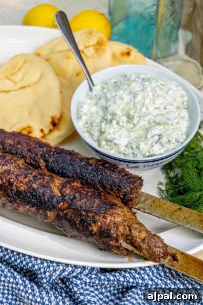 Effortless Griddled Greek Gyros 2 Two Greek gyros on skewers served on a plate with fresh tzatziki sauce and warm pita bread.