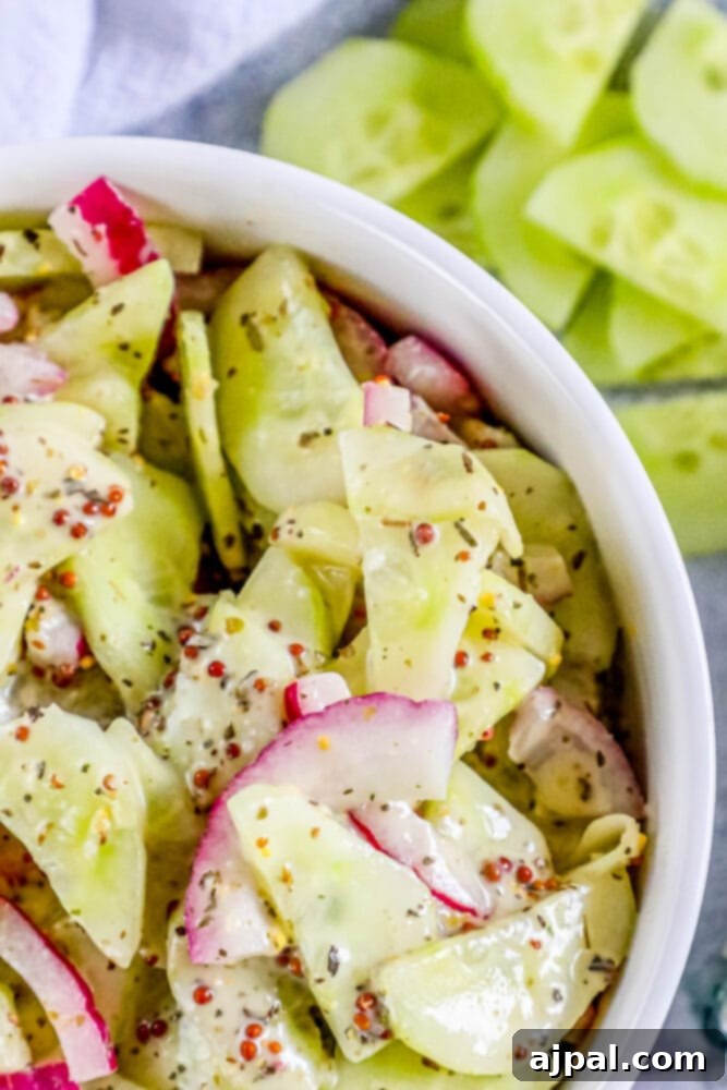 Cool Creamy Cucumber Salad 3 Top-down view of a creamy cucumber salad with visible red onion slices and mustard seeds in a white bowl, ready to be served.