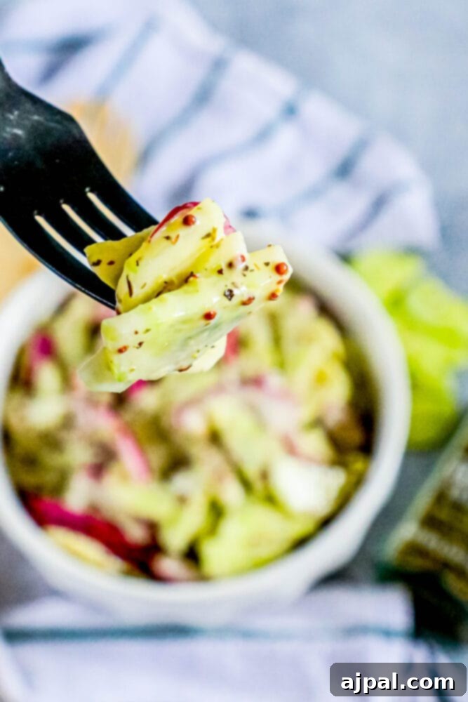 Cool Creamy Cucumber Salad 4 A fork lifts a generous portion of creamy cucumber salad, showcasing the thinly sliced cucumbers, red onions, and creamy dressing.