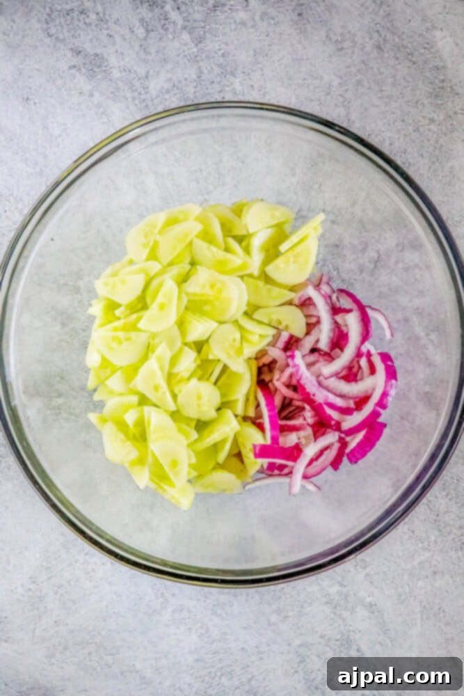 Cool Creamy Cucumber Salad 6 Sliced cucumbers and finely diced red onions are combined in a large glass bowl, representing the initial step in preparing creamy cucumber salad.