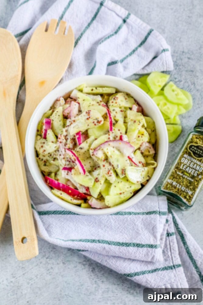 Cool Creamy Cucumber Salad 9 A white bowl filled with creamy cucumber salad, featuring visible slices of cucumber and red onion, with a wooden spoon resting beside it.