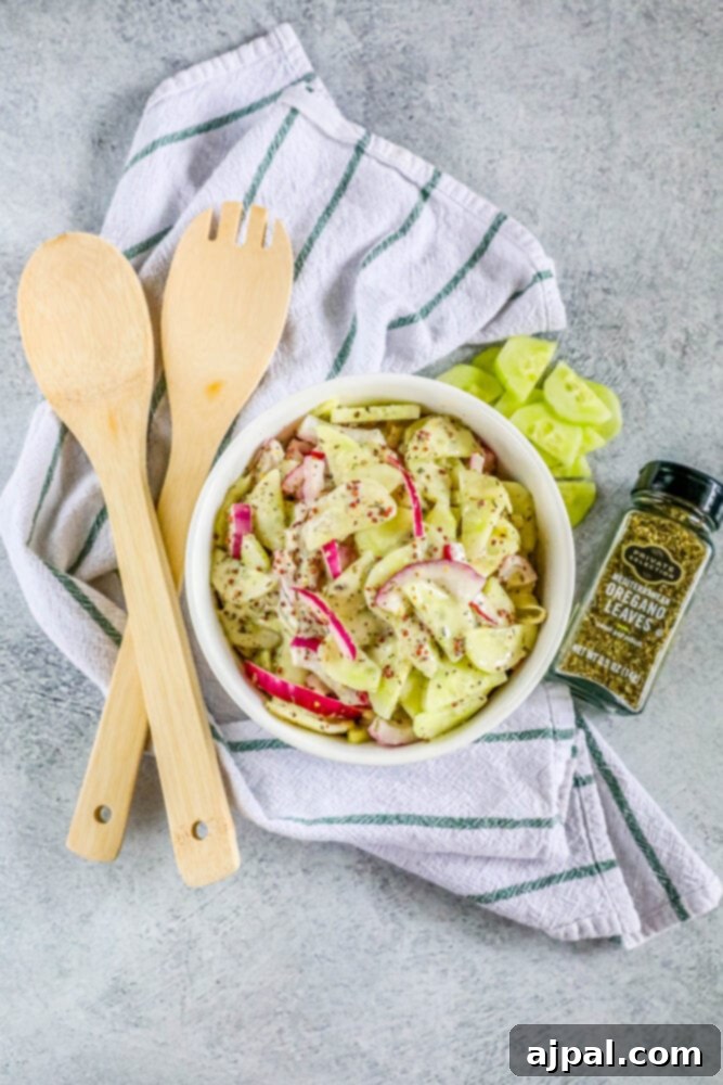 Cool Creamy Cucumber Salad 10 A white bowl brimming with creamy cucumber salad, garnished with fresh herbs, and two wooden serving spoons nestled within, ready for a gathering.