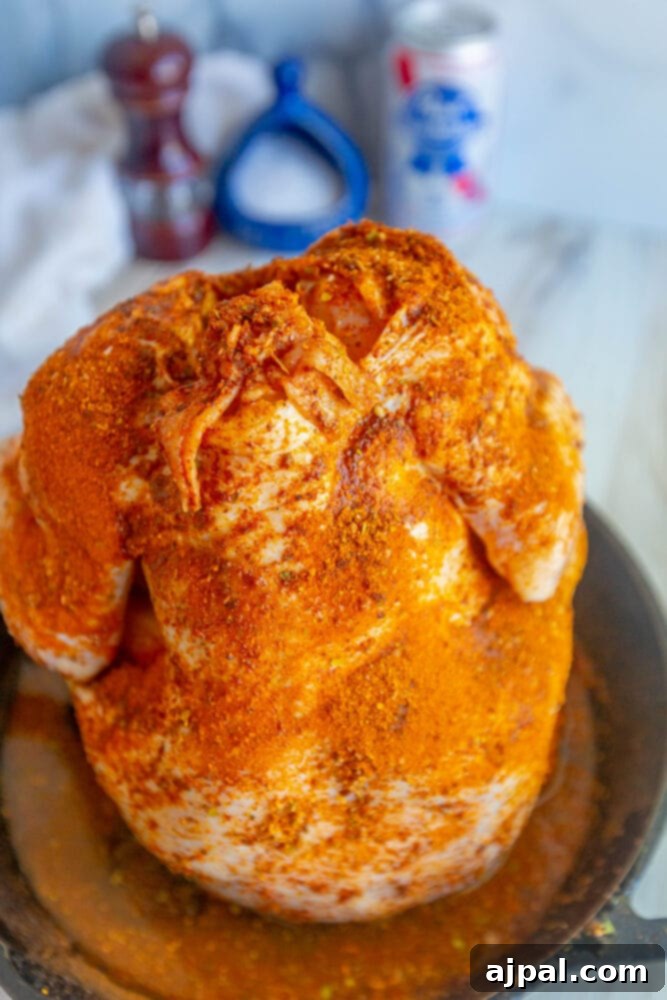 seasoned raw whole chicken with a beer can in the cavity on a cast iron pan