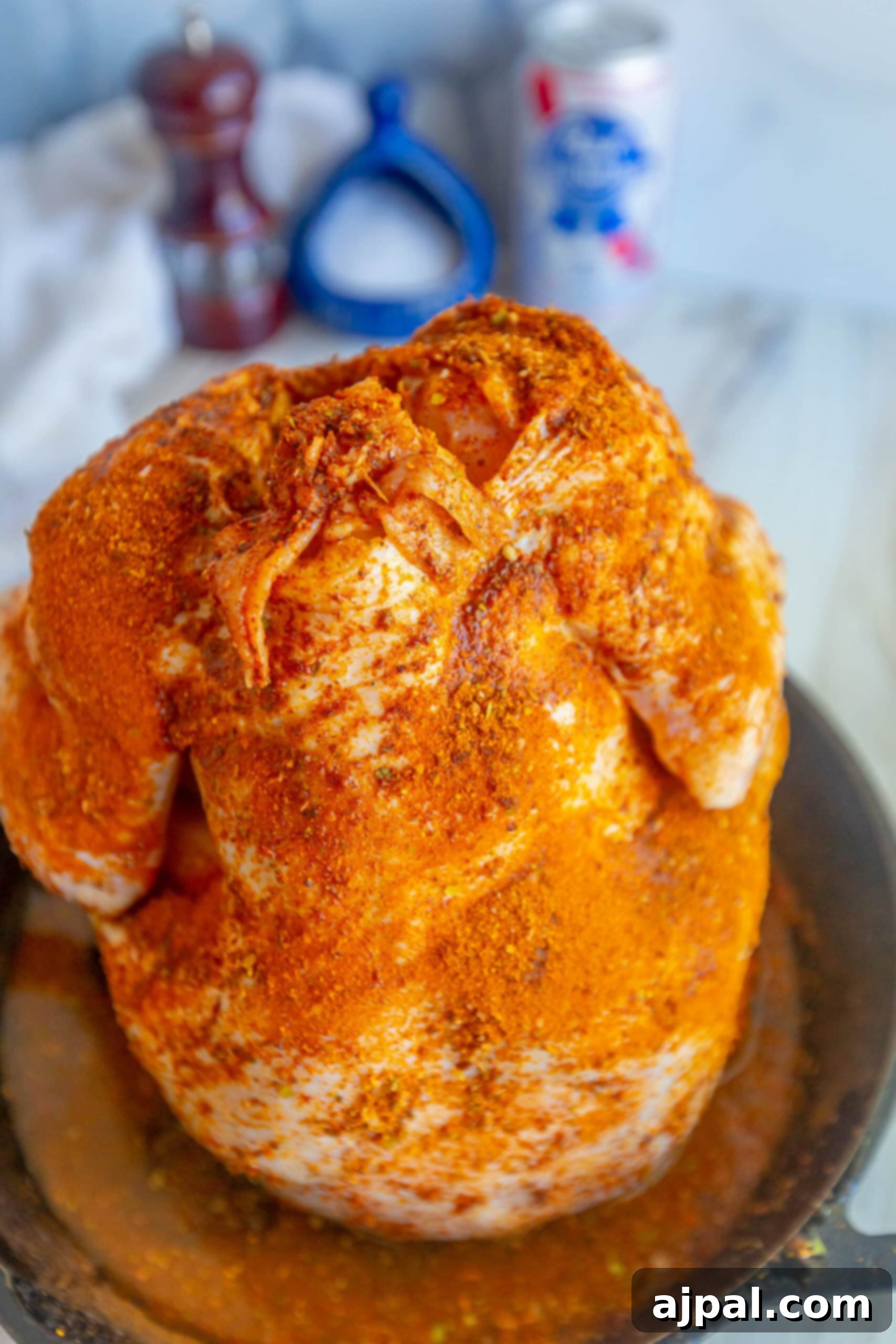 seasoned raw whole chicken with a beer can in the cavity on a cast iron pan