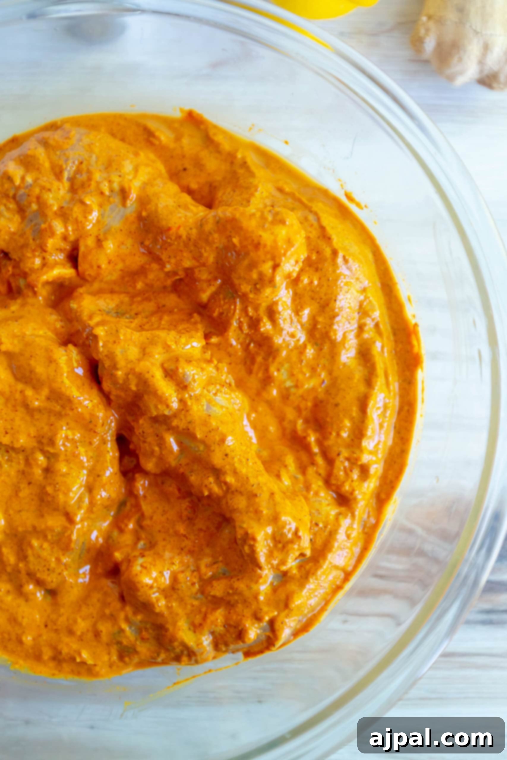 Chicken pieces thoroughly coated in a rich, reddish tandoori marinade in a large glass bowl, ready for chilling.