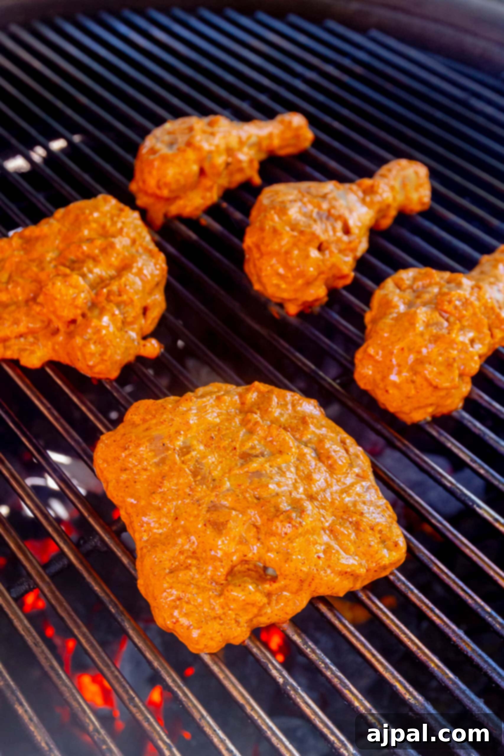 Reddish tandoori chicken pieces sizzling on a hot outdoor grill, creating smoky char marks.