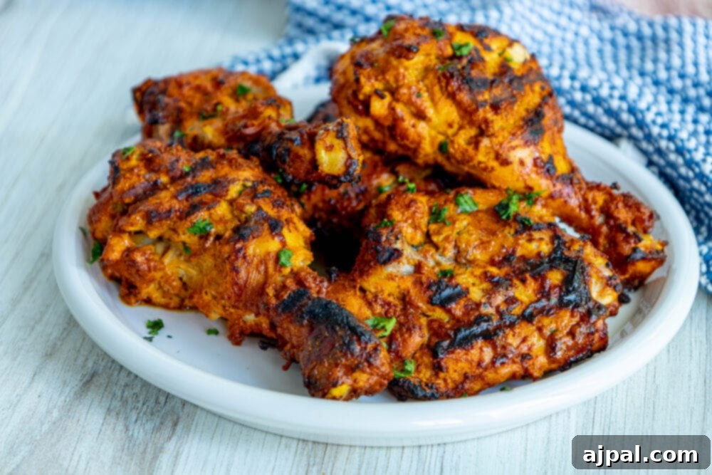 A serving of grilled tandoori chicken thighs on a white plate, garnished with finely sliced green onions for freshness.